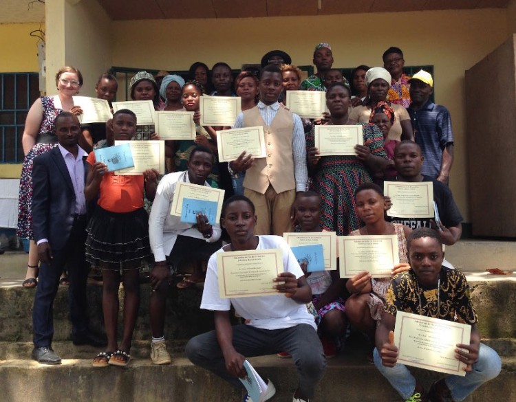 A group of young people in Campo, Cameroon, posing on the steps of a building and holding up certificates.