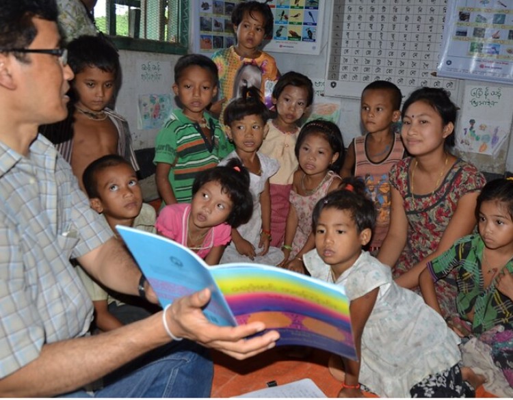 A man reads a story book to a group of small children in the Chittagong Hill Tracts, Bangladesh