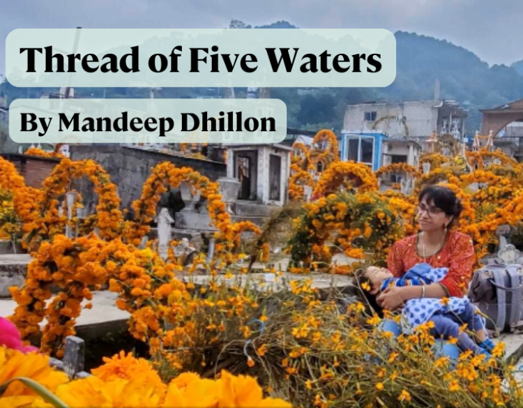 Photo of a square draped with marigold garlands. In the middle is sitting a woman holding a sleeping child. 