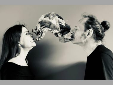 Photo of two people with a twisted paper "speech bubble" emerging from their mouths