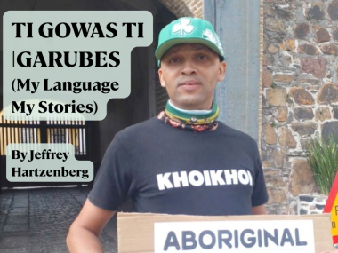 A photo of Jeffrey Hartzenberg, a young man wearing a green baseball cap and a black t-shirt that says "KHOIKHOI". He is holding a cardboard sign, of which only the top word is visible: "ABORIGINAL". Text to his left reads: "TI GOWAS TI |GARUBES (My Language My Stories), by Jeffrey Hartzenberg"