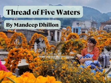 Photo of a square draped with marigold garlands. In the middle is sitting a woman holding a sleeping child. 