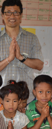 Dr. Maung Nyeu stands behind three school children, all folding their hands in greeting 