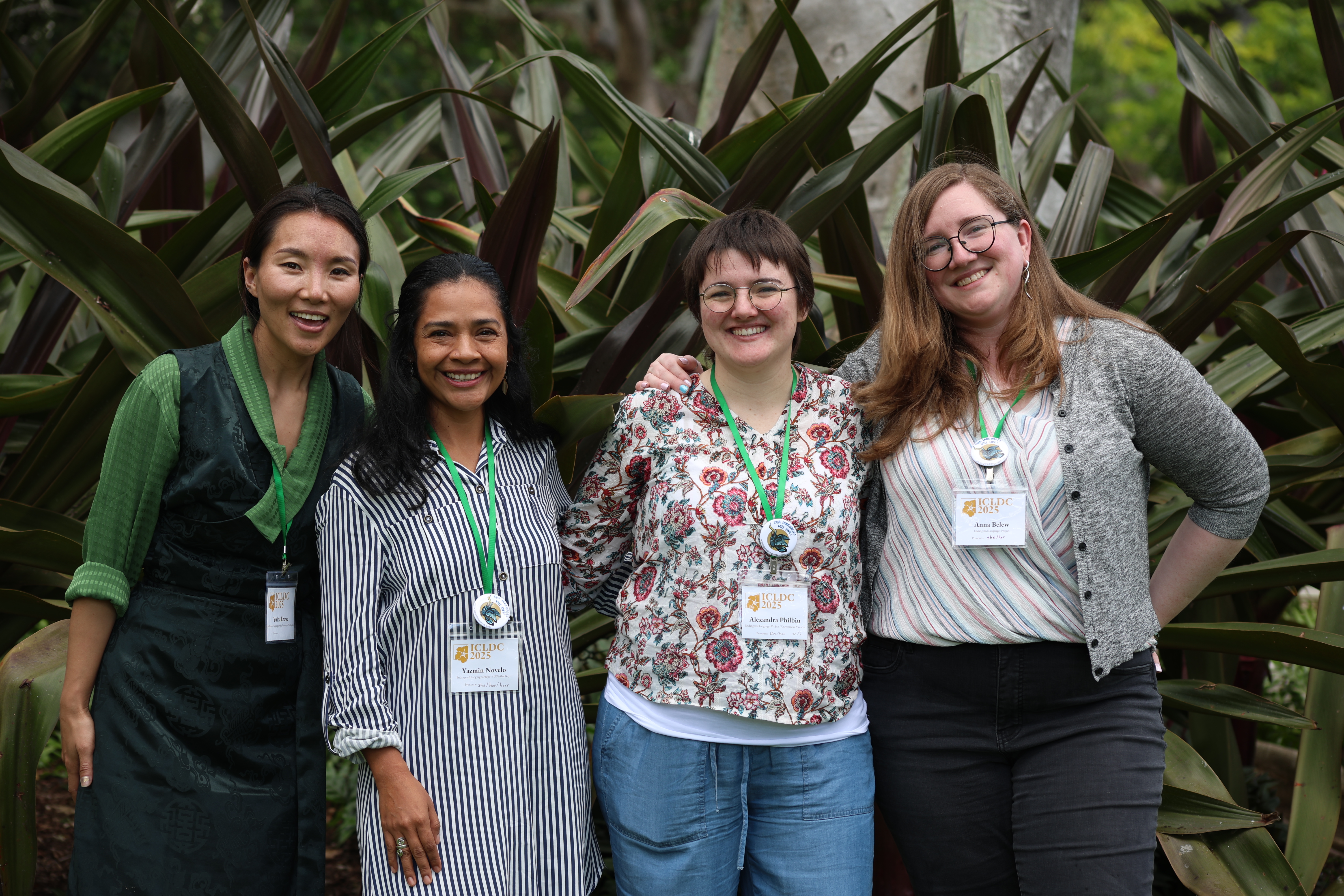 Four women standing in front of a large spiky plant, with their arms around each other and smiling