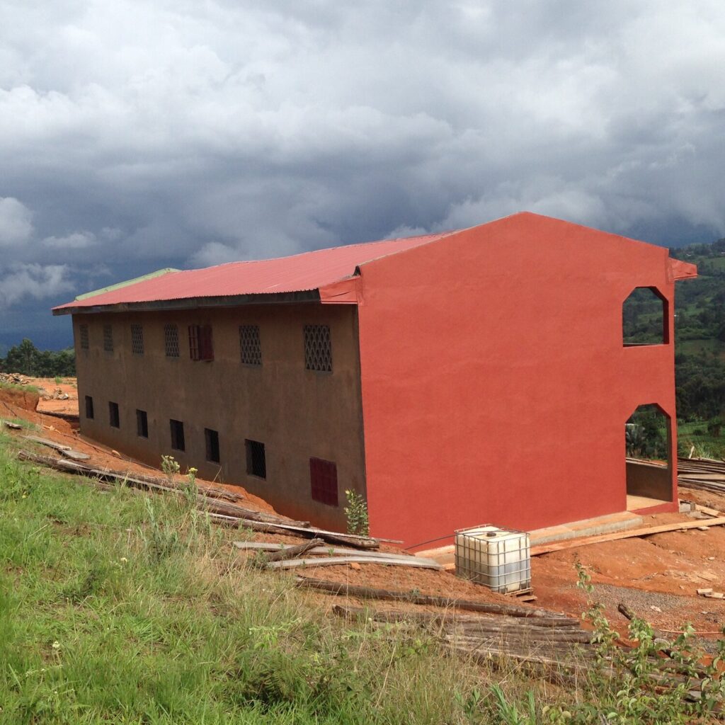 A bright red two-story school building, against green mountains and a cloudy sky.
