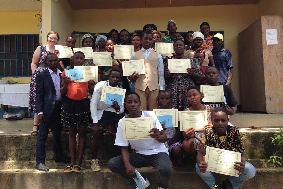 A group of young people and their families in Campo, Cameroon, posing on the steps of a building, holding up certificates