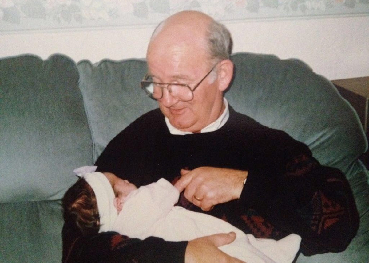 An older man looking down at a baby he is holding.