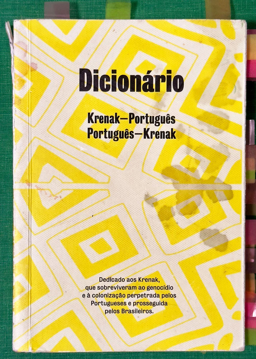 A photo of the bright yellow patterned cover of the Krenak dictionary. The cover is tattered and stained from use.