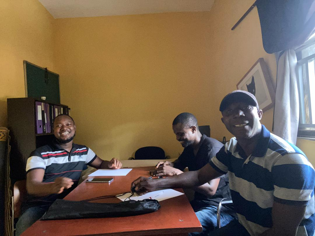 Three men sitting at a table with documents in front of them, all smiling
