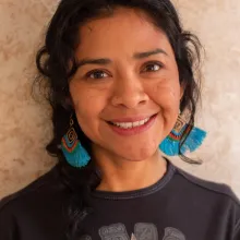 A Mayan woman with chin-length hair, wearing turquoise earrings and a black shirt, smiling