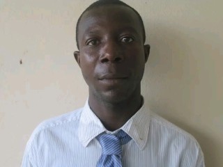 A man in a blue collared shirt and tie looking at the camera. 