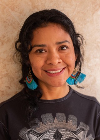 A Mayan woman with chin-length hair, wearing turquoise earrings and a black shirt, smiling
